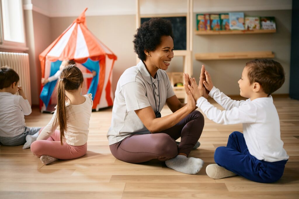 Happy black PE teacher and small boy having fun during exercise class at preschool.